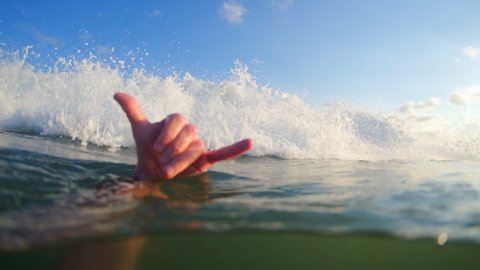 Hand with the Shaka sign and breaking ocean wave