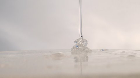 A trickle of clear cosmetic gel with tiny bubbles drips onto the surface. facial serum, anti-aging cream, hair shampoo, antibacterial gel, hyaluronic acid