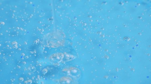 A trickle of clear cosmetic gel with tiny bubbles drips onto the blue surface. facial serum, anti-aging cream, hair shampoo, antibacterial gel, hyaluronic acid