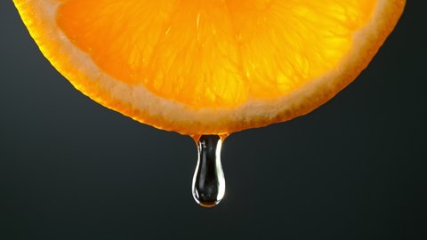 Super Slow Motion Macro Shot of Water Drop Falling from Fresh Orange Slice on Black at 1000fps.