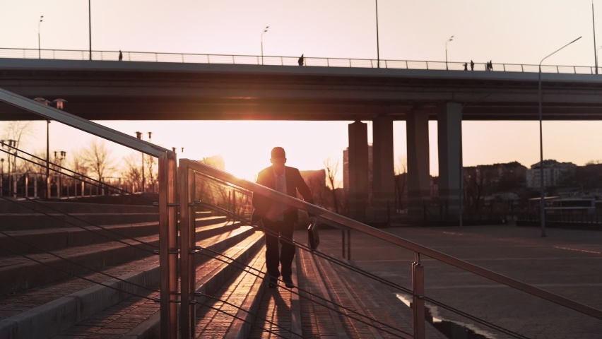 Businessman in jacket and tie with a suitcase in his hands jumps over an obstacle on background city in the sunset light. Office worker makes a trick through parapet. Concept overcoming difficulties. Royalty-Free Stock Footage #1069985527