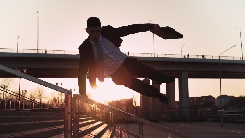 Businessman in jacket and tie with a suitcase in his hands jumps over an obstacle on background city in the sunset light. Office worker makes a trick through parapet. Concept overcoming difficulties. | Shutterstock HD Video #1069985527
