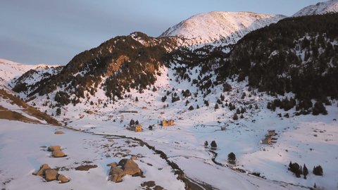 Smooth drone traveling through the snowy town of Cortals in Andorra, with the last lights of the day. In the background the mountains of Encamp.