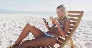 Animation of heart digital icons over woman in deckchair using smartphone on beach. digital interface, social media and global technology concept digitally generated video.
