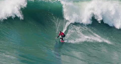 NAZARE, PORTUGAL - 07 FEBRURARY, 2021: Man surfing big waves at Nazare beach, Portugal, Europe. Nazare point - famous place of largest waves in world. 4k footage in slow motion