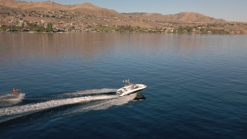 Watersports Aerial Video of Summer Fun Wakeboarding Behind Boat on Lake Chelan. Man riding board behind speedboat with drone following Royalty-Free Stock Footage #1069999051