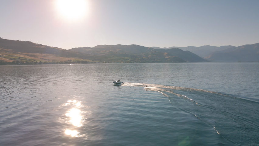Sunny Summer Day Aerial of Wakeboarding Behind Boat on Lake Chelan. Drone video of man riding board behind boat in beautiful sunshine Royalty-Free Stock Footage #1069999144