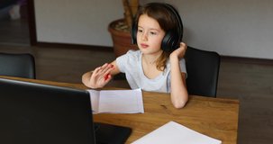Cute little girl with headphones using laptop to study at home, writing, answer, online learning, education, social distance, quarantine coronavirus.