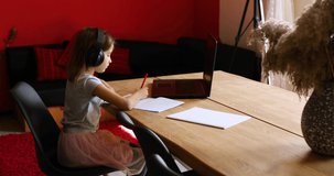 Little girl with headphones writing and using laptop to study at home, mother come and help her, online learning, education, social distance, quarantine coronavirus.