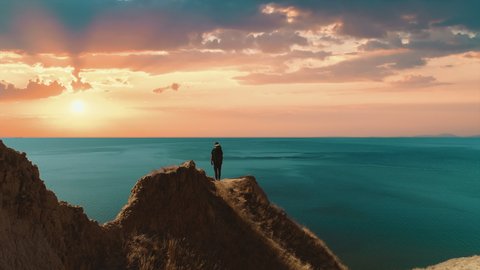 The man with bag standing on the mountain cliff on the seascape background