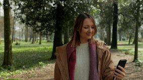 Young woman walking in park having video call on smartphone