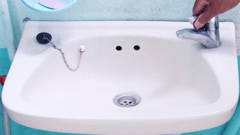 man hand turn on chrome faucet and water flowing in wash basin, after that man hand turn off chrome faucet in the bathroom