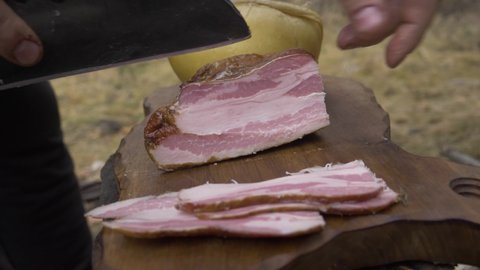 Traditional Satar knife cuts pork ham in nature, on an old oak chopper. The location is in the mountains for a winter time.