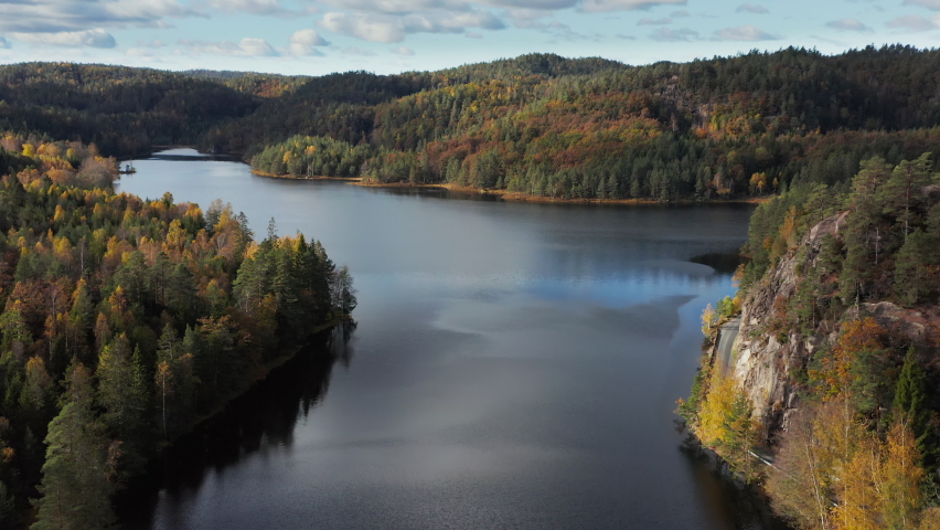 Aerial view of a lake, surrounded by mountains and autumn color forest, in Norway - tilt up, drone shot