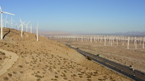 Drone flying sideways overlooking highway inbetween of huge wind farm and wind turbines near Palm Springs in the Mojave Desert, California, USA.