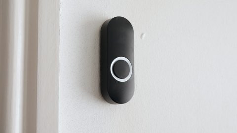 Apartment door bell being pressed. A woman presses a black doorbell with her finger on a white wall.