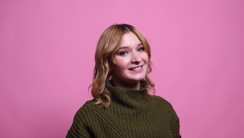 Young woman smiles and straightens her hair in the studio on a pink background