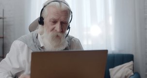 Senior Retired Man with Headset looking at Laptop screen talking Distance. Having Online Conversation at home with family using Modern Device. Spending time while Quarantining. Communication.