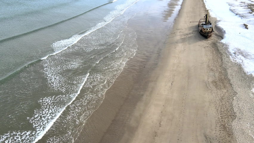 Aerial Top view of old wrecked fishing ships drowned at the sea shore in snowy winter season. Footage. Aerial view of the ruined boat in the cold water of Barents sea in Teriberka, Russia
