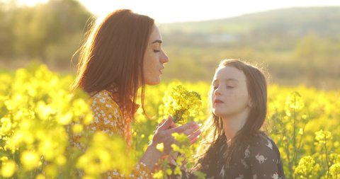 Red Haired mom gently hugs her little cute daughter. Walk against the background of rapeseed field. Mother day concept.