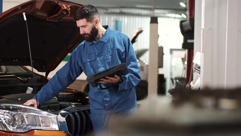 Professional auto mechanic examining car engine, looking under hood