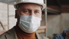 Close up portrait of professional male architect in face mask and helmet looking at camera with confidence while posing at construction site during covid-19 pandemic - Powered by Shutterstock - Get 15% off with code: PIKWIZARD15