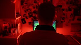 Back view of unrecognizable pro gamer sitting in dark room illuminated with red neon light and playing RPG cyber video games and holding tournaments with virtual players on powerful PC. Virtual