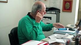 Senior man working in office room with documents, files and papers, man using modern wireless headphones while working. Financial calculations in trading, manager checking data and figures - Powered by Shutterstock - Get 15% off with code: PIKWIZARD15