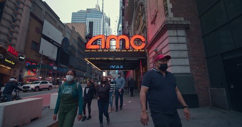 New York, New York  United States - March 29, 2021: People wearing masks walk in front of the recently re-opened AMC Movie Theater in Times Square.