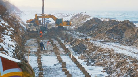 A working process of construction on the seashore in winter. Builders with excavators are working under the snowfall. Strengthening the embankment or building a coastal promenade