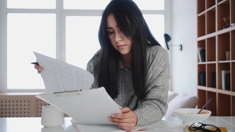 A focused asian woman is working with paper documents sitting at the apartments