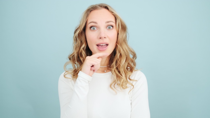 A surprised woman is thinking about something while coming-up with an idea standing isolated over blue wall in a studio