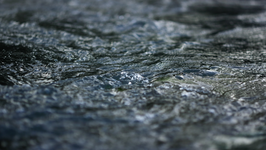 Mountain river water surface in slow motion. Clear stream making waves in mountain river. Closeup flowing water background. Rapid flow running through stone rapids. Close up of mountain river. Royalty-Free Stock Footage #1070039089