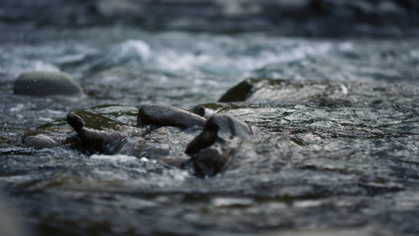 Beautiful water surface in slow motion. Close up of flowing river water with stones in mountains. Rapid stream of water in mountain river. Scenic view of wild rocky rapids 