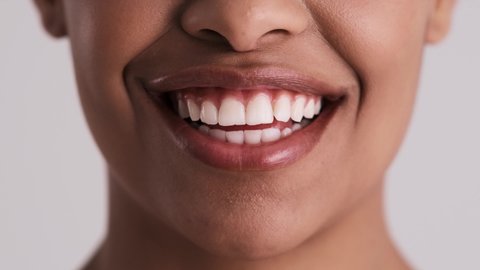 A close-up cropped view of a young woman's mouth isolated over a gray background in the studio