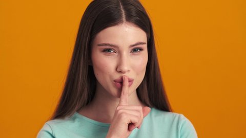 A pretty nice young woman is showing silence gesture standing isolated over orange background in the studio