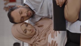 A pregnant Muslim woman wearing a headscarf and her husband use a tablet computer to exchange babies online Online baby shopping concept.Video for the vertical story.