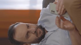 Young bearded man reading news or messages on his mobile phone at home.The young man is surprised at the news he saw, laughing.Video for the vertical story.