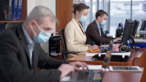 Blurred Caucasian man sneezing in office and colleagues in Covid-19 face masks leaving workplace. Scared man and woman walking away from coworker with symptoms of infectious respiratory disease
