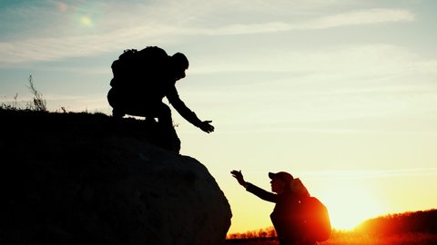 Helping Hand. Man giving hand a teammate to help her to climb the mountain. Help and assistance, hand reaching out to help friend at beautiful sunset sky. Hiking and team work concept. People helping.