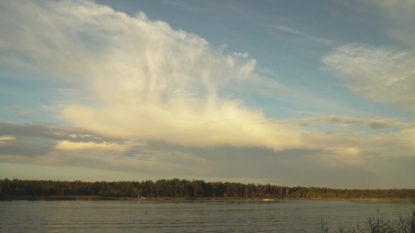 Large cumulus clouds in a panoramic view over the lake in the evening. The picturesque landscape of heaven above the water surface in the summer season. Recreation place with a water scooter rider.