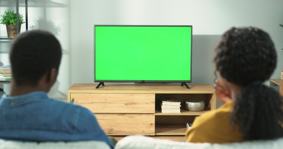 Back view of young African American family couple watching TV with chroma key while resting at home sitting on sofa in room. Wife and husband spending time together watch television with green screen | Shutterstock HD Video #1070048671