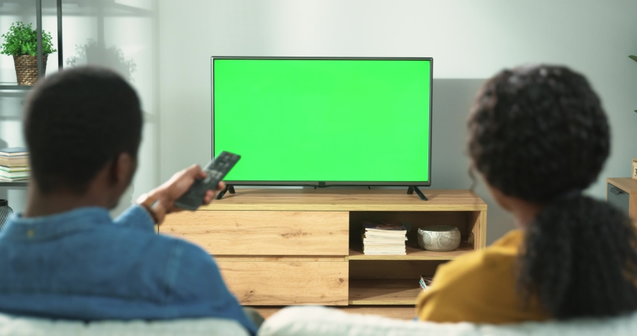Back view of young African American family couple watching TV with chroma key while resting at home sitting on sofa in room. Wife and husband spending time together watch television with green screen Royalty-Free Stock Footage #1070048671