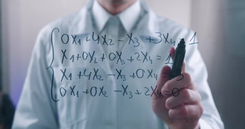 Male scientist thinks over the solution of the equation, drawn on a glass board in a laboratory. The mathematician solves the problem.