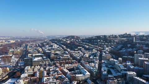 Aerial panning and tilting across beautiful city skyline with red tile roofs, streets and mountains covered in snow during winter in Stuttgart, Germany.