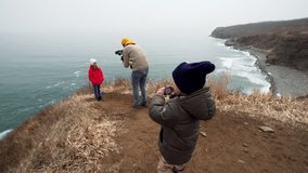 4 years old boy is taking photo or video of marine landscape. Father is filming his daughter walking on the cliff edge