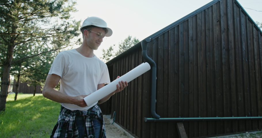 Blanc is in the hands of a young enthusiast who stands in a protective helmet near a built wooden house and is pleased with the work amid the warm summer sunset.