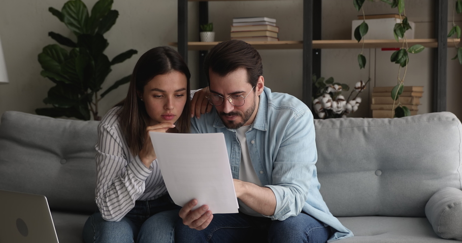 Young stressed married couple sit on couch hold papers reading bad news in legal document, got warning notice feel shocked looking frustrated. Pay penalty, unpaid debt, eviction notification concept | Shutterstock HD Video #1070064784
