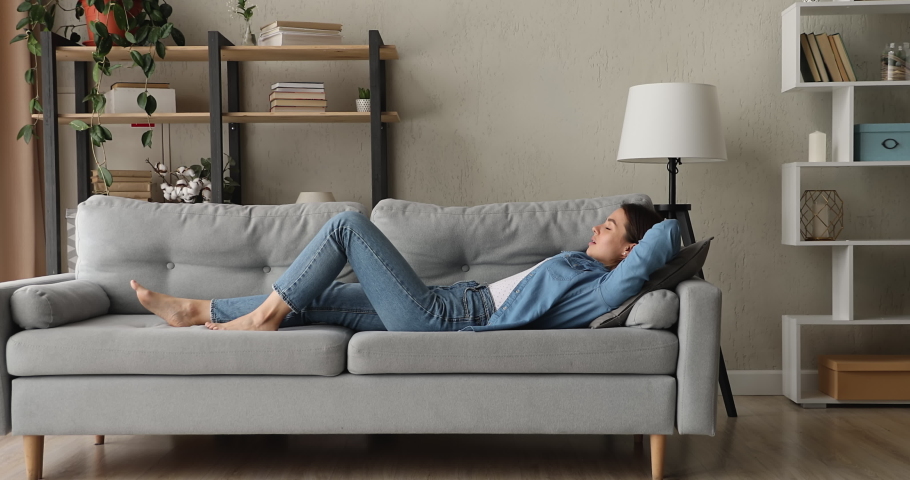 Side full length view woman with eyes closed put hands behind head lying on comfy couch breathing fresh conditioned air take break enjoy stress-free day alone in modern living room. Relaxation concept Royalty-Free Stock Footage #1070064937