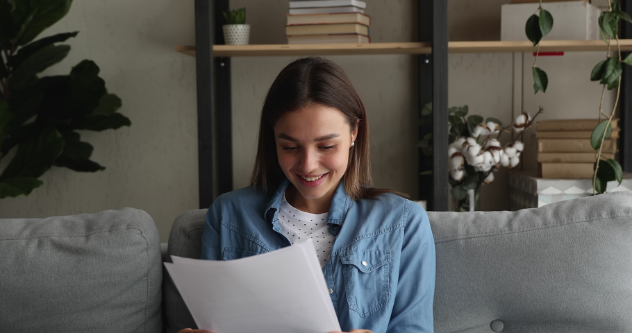 Attractive woman sit on sofa hold in hands sheets read great news in letter feels happy celebrate success. University admission, scholarship got, career growth and advance, bank loan approved concept Royalty-Free Stock Footage #1070064988